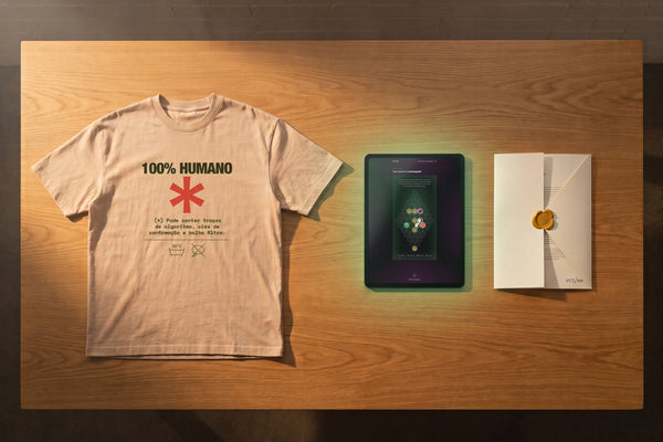 Fotografia editorial com uma camiseta EXALLAXE oversized nude exibindo a estampa Decomposition Label, um tablet com o Painel Exallaxe mostrando Aferições adquiridas desbloqueadas, e uma carta de fundação aberta com selo de cera mostarda.
